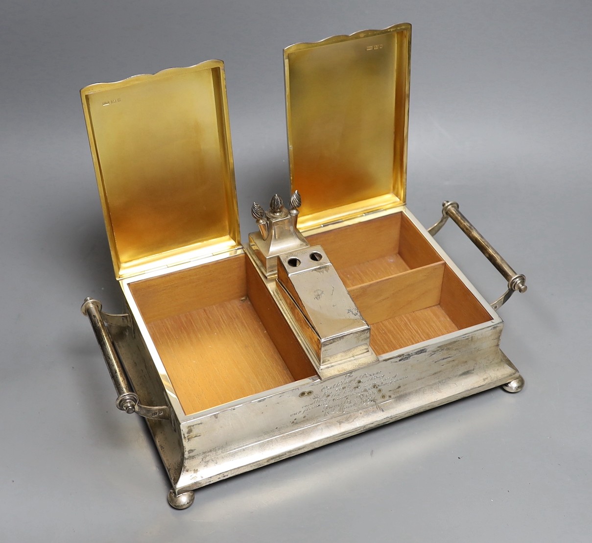 A George V silver mounted two handled desk top twin cigarette box incorporating a cigar cutter and lighters, with 1957 presentation inscription, Mappin & Webb, London, 1926, width 33.5cm.